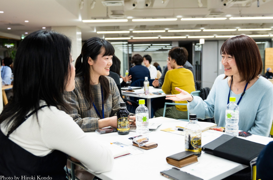 明るいイベントスペースで、3人の女性がテーブルを囲み、笑顔でいきいきと会話を楽しんでいる写真。