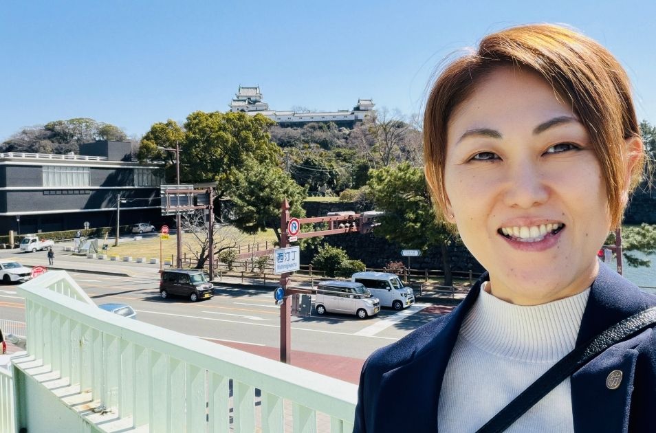 青空の下、遠くにそびえる立派なお城(和歌山城)を背景にして、橋の上で笑顔で自撮りをする進絵美さんの写真。