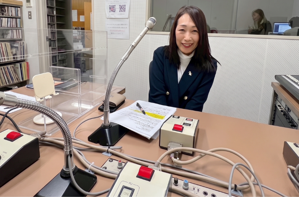 ラジオ局のスタジオで、マイクの前に座り笑顔で原稿に目を通す古池さんの写真。