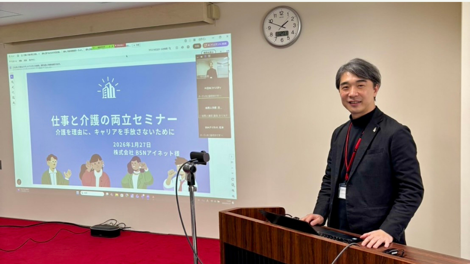 『仕事と介護の両立セミナー』と映し出されたスクリーンを背景に、演台に立ち笑顔でカメラに目線を送る川上洋平さんの写真。