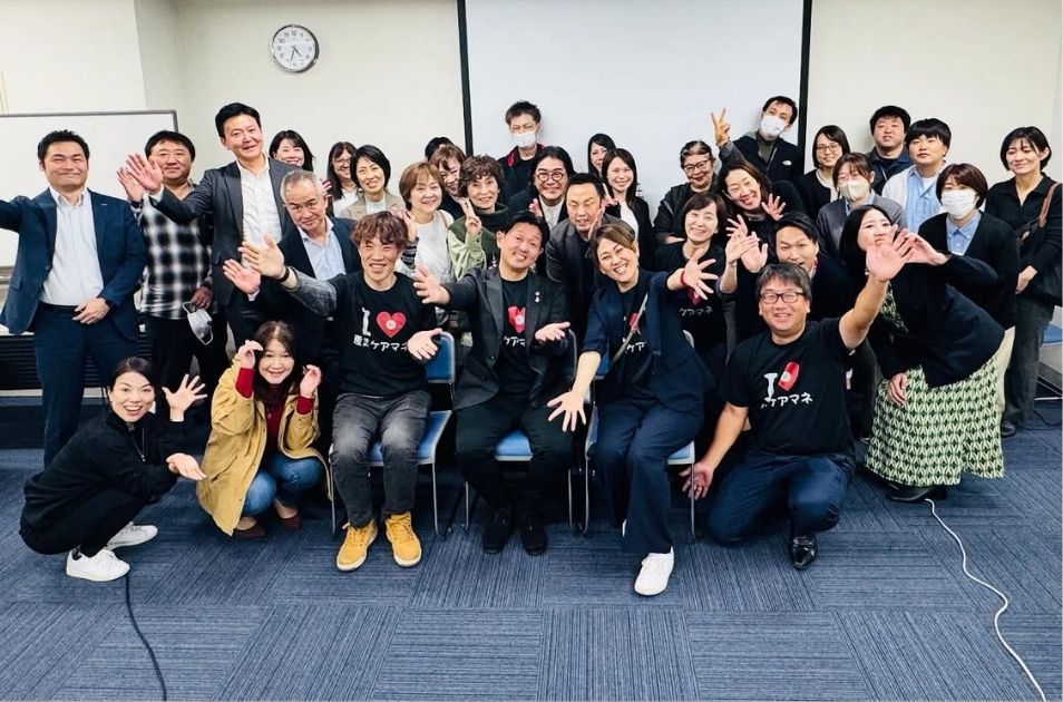 お揃いの『I LOVE ケアマネ』Tシャツを着た参加者たちと共に、和やかな笑顔を見せる集合写真