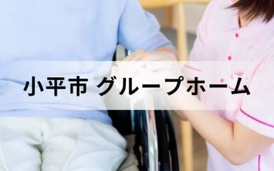 介護コラム：小平市のグループホーム事情。ピンクのユニフォームを着た介護スタッフが、車椅子に乗った高齢者の手を優しく握っている安心感のあるイメージ。