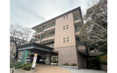 レンガ調のタイル貼りが特徴的な、「特別養護老人ホーム文京千駄木の郷」などが入る複合施設の外観写真。手前には大きな車寄せがあり、送迎車が停まっている。