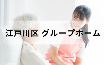 介護コラム：江戸川区のグループホーム事情。ピンクのエプロンを着た若い介護スタッフが、笑顔で高齢者に語りかけている安心感のあるイメージ。