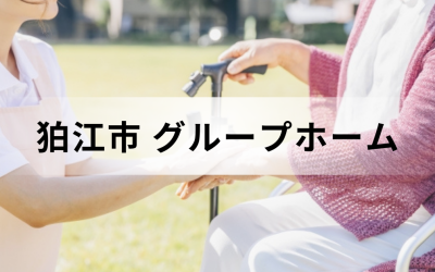 東京都狛江市のグループホーム。日差しの温かい屋外の芝生で、車椅子に乗った高齢者の手を優しく握る介護スタッフの安心感のあるイメージ。
