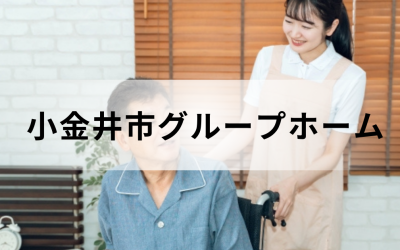 介護コラム：小金井市のグループホーム事情。ベージュのエプロンを着た笑顔の介護スタッフと、車椅子に乗った高齢男性の温かいイメージ。