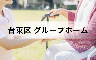 介護コラム：台東区のグループホーム事情。日差しの温かい屋外の芝生で、車椅子に乗った高齢者の手を優しく握る介護スタッフの安心感のあるイメージ。