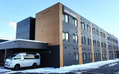 移住ニーズに応える特定施設「ふれあいの里 蒼華（あおば）」の外観。雪景色の中に建つ、黒とブラウンのモダンな3階建て建物の写真。