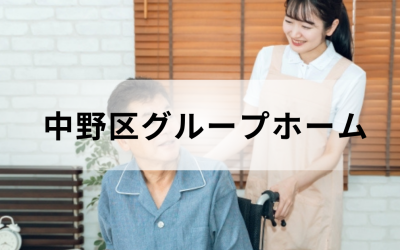 介護コラム：中野区のグループホーム事情。ベージュのエプロンを着た笑顔の介護スタッフと、車椅子に乗った高齢男性の温かいイメージ。