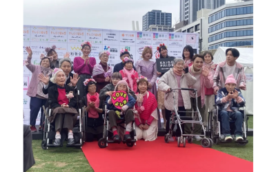 屋外イベントで、ピンク色の服や小物を身につけて笑顔で並ぶ利用者とスタッフの集合写真