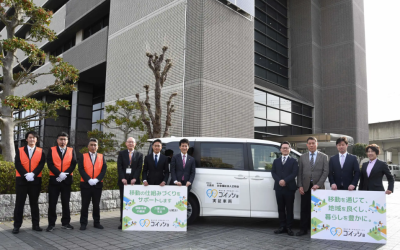兵庫県川西市とダイハツ工業が連携して行う、AIを活用した福祉介護・共同送迎サービス「ゴイッショ」の実証実験出発式の様子。市役所前に停まる送迎車両と関係者の集合写真。