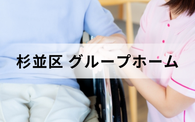 介護コラム：杉並区のグループホーム事情。ピンクのユニフォームを着た介護スタッフが、車椅子に乗った高齢者の手を優しく握っている安心感のあるイメージ。